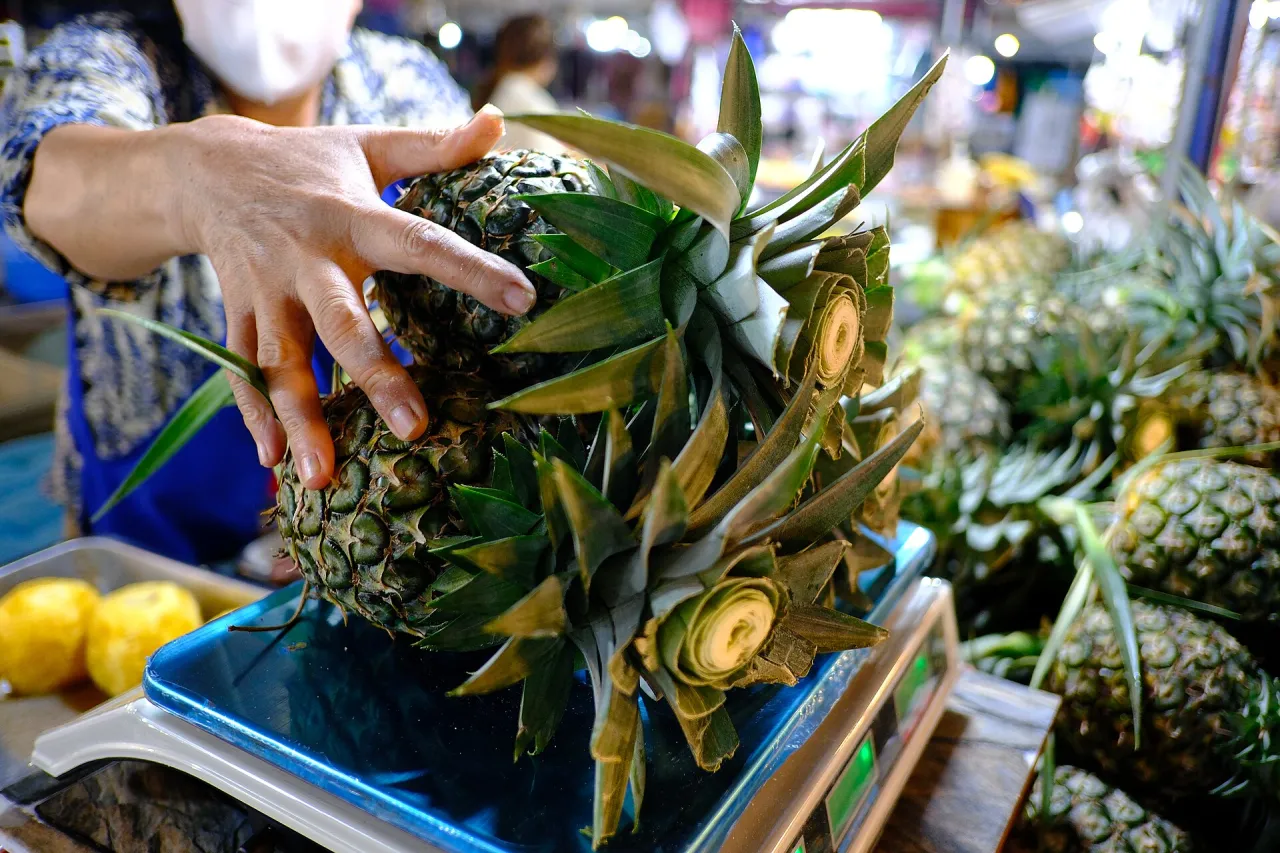 Vendor weighing a pineapple at a market stall